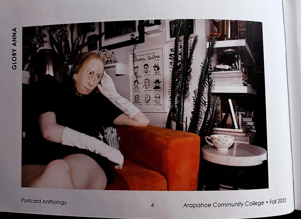 The photograph shows a masked person wearing a black dress and long white gloves lounging on a red comfy chair. Next to the red comfy chair is a cup of tea on a small table.